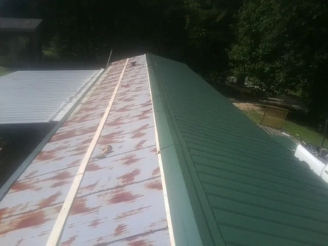 Old rusted panels beside newly installed green metal roofing — Wind Damage Roof Repair by Roofing Brothers in Clinton